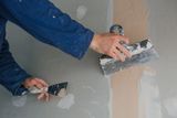 Hände mit Glättkelle und Spachtel beim Verspachteln einer Gipskartonwand