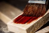 Pinsel trägt rotbraune Holzschutzlasur auf ein Holzbrett auf