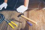 Hände in Arbeitshandschuhen mit Hammer, Zange und Werkzeug auf Holzboden